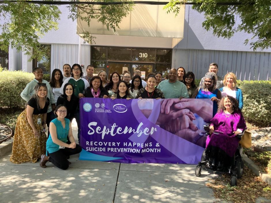 Photo of 2023 Suicide Prevention Committee. Holding a Suicide Prevention Month and Recovery Happens Month banner.