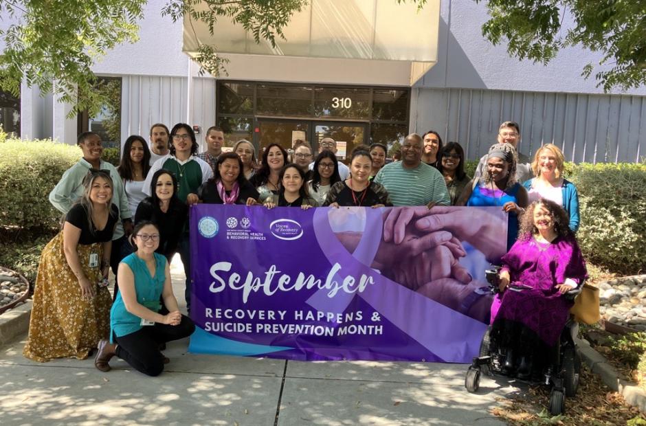 Photo of 2023 Suicide Prevention Committee. Holding a Suicide Prevention Month and Recovery Happens Month banner.